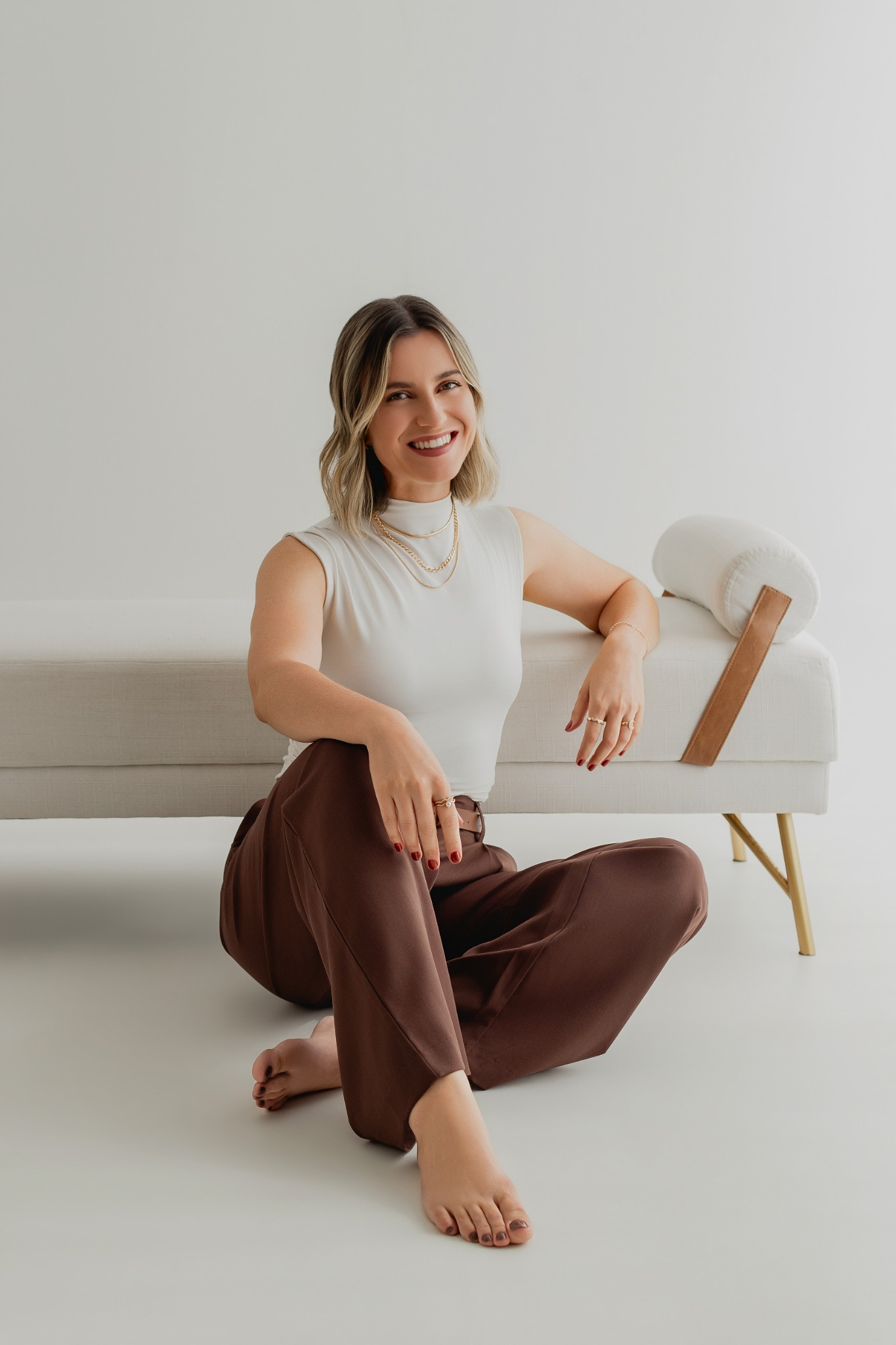 Retrato profissional da Psicóloga Joselma Colares sentada no chão, de pés descalços e com calça marrom